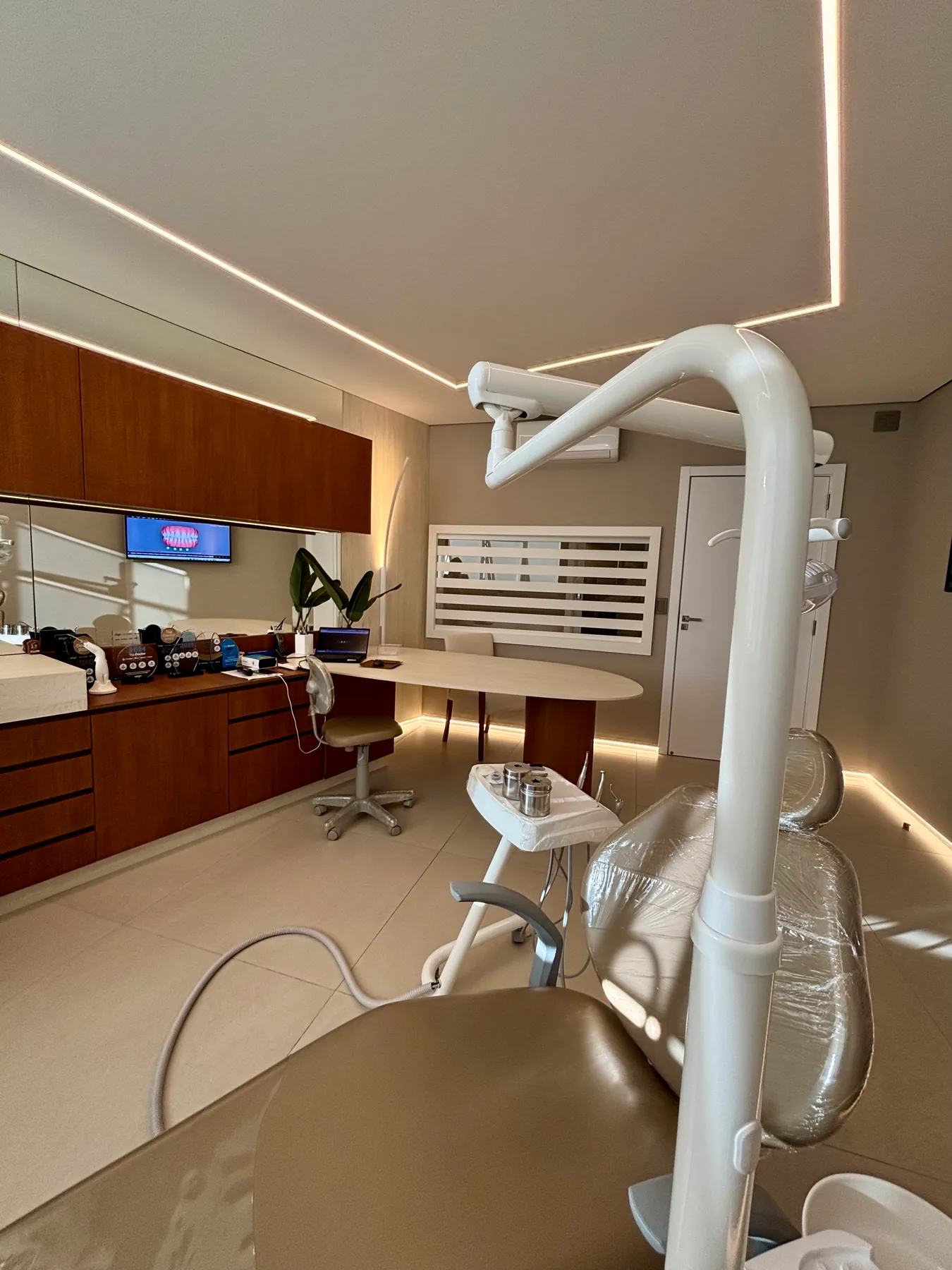 Vista da sala de atendimento da Dra. Roberta, com cadeira odontológica, bancada e iluminação no teto.